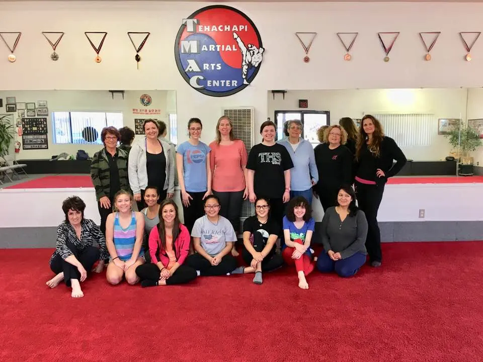 A group of women and girls from a TRU class posing together on the red mat.